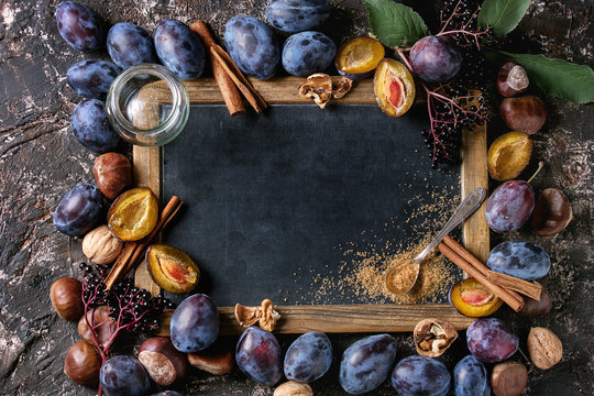 Autumn frame from plums, nuts, cinnamon, glass jar and brown sugar with empty vintage chalkboard over brown concrete background. Top view with space for text. Fall harvest and jam making concept.