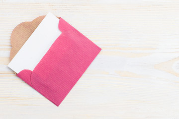 Top view of pink envelope with empty card – copyspace for your text on light wooden background