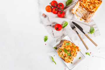 Italian food recipe. Dinner with classic lasagna bolognese with béchamel sauce, parmesan cheese, basil and tomatoes, on white marble table, coopy space