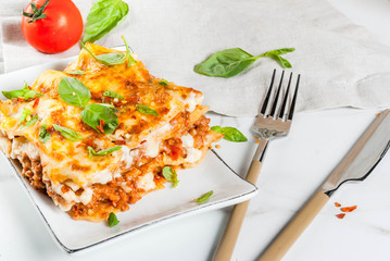 Italian food recipe. Dinner with classic lasagna bolognese with béchamel sauce, parmesan cheese, basil and tomatoes, on white marble table, coopy space