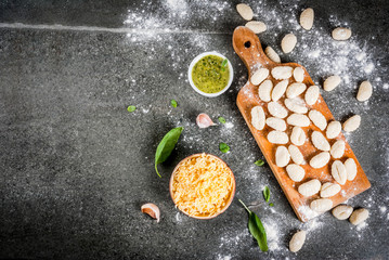 Raw uncooked homemade potato gnocchi with flour, grated parmesan cheese, basil and pesto sauce. On concrete grey background, copy space top view