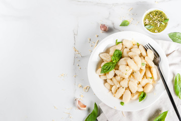 Italian food recipe, Healthy vegan dinner with potato gnocchi. With grated parmesan cheese, basil and pesto sauce. On white marble , copy space  top view