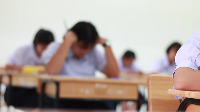 blurred of Female students wearing school uniform Concentrating on doing tests and taking exercises exams on wooden tables and chairs in secondary schools classroom Thailand, Educational concepts