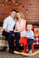 Portrait of happy family: smiling little boy sitting on a wooden horse in the decorated room. Concept of Merry Christmas and Happy New Year