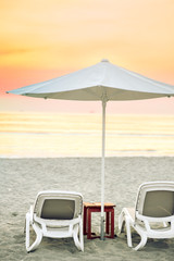 Two sun beds and an umbrella on sandy beach. Scenic sunset over Adriatic Sea