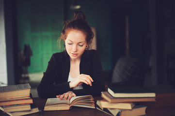indoor portrait of beautiful redhead woman learning or reading books in university or library