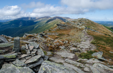 Fototapeta premium Hiker walks the stony road on the mountain ridge with a former Polish-Czechoslovak border column in the foreground