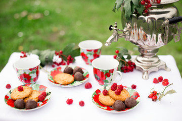 Самовар с чашками и десертом с малиной на столе в саду. Завтрак на природе 