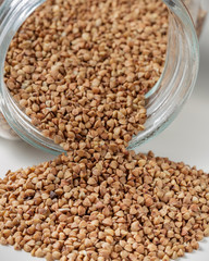 Uncooked buckwheat scattered from jar on table