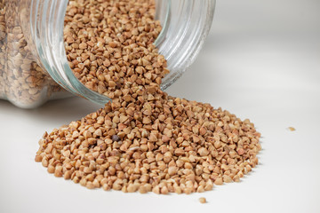 Uncooked buckwheat scattered from jar on table