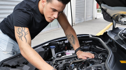 Plakat Handsome young man trying to repair a car engine, looking inside open bonnet