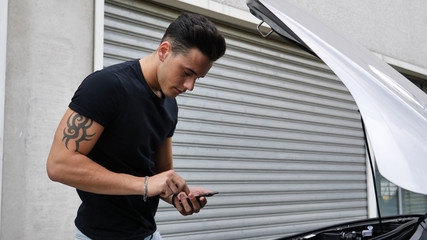 Fototapeta premium Young man trying to repair a car engine and seeking help with cell phone calling a mechanic