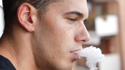 Handsome man standing on balcony and vaping with electronic cigarette.
