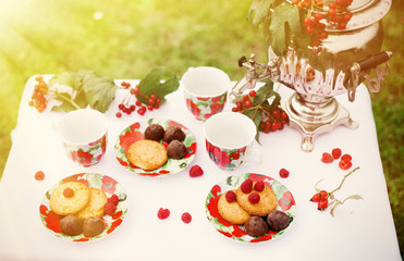 Утренний завтрак в саду. Самовар, блюдца, чашки стоят на столе. Печенье, конфеты, малина на завтрак