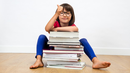 smiling child sitting behind many books with a thumbs up