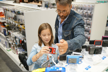 Obraz premium Man with kid looking at compact cameras in multimedia store