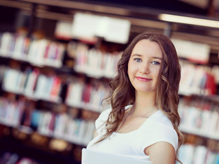 Happy female student holding books at the library