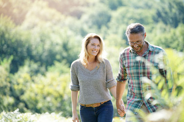 Happy mature couple walking in countryside on sunny day - Powered by Adobe
