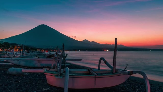 Sunset overlooking the Agung volcano timelapse on the background of fishing boats on the beach of Djemeliuk in Amed on the island of Bali in Indonesia.