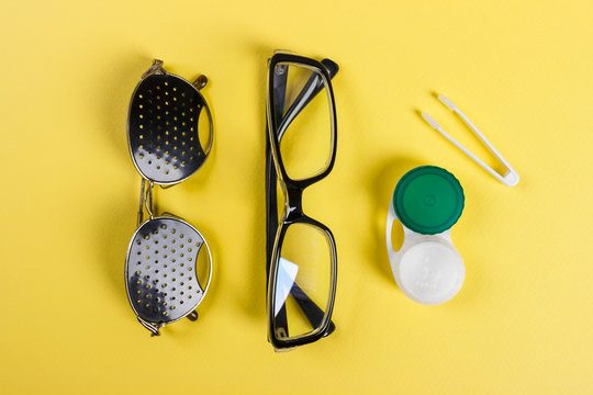 A set of accessories for sight. Pinhole glasses, lenses with container and glasses for sight. Pair of medical pinhole glasses with reflections. Medical concept. Top view