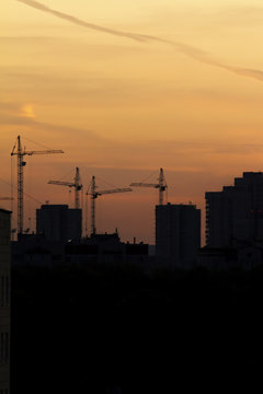 Construction cranes near residential apartments - view on sunrise, vertical