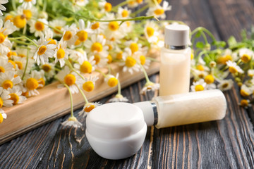 Jar and bottles with cream and chamomile flowers on wooden table