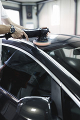 Naklejka premium Car detailing - Hands with orbital polisher in auto repair shop. Selective focus.