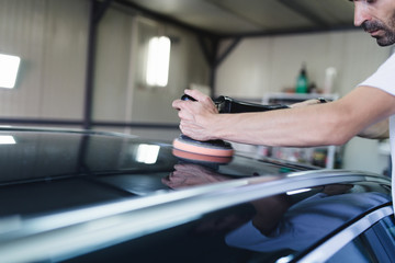 Car detailing - Hands with orbital polisher in auto repair shop. Selective focus.