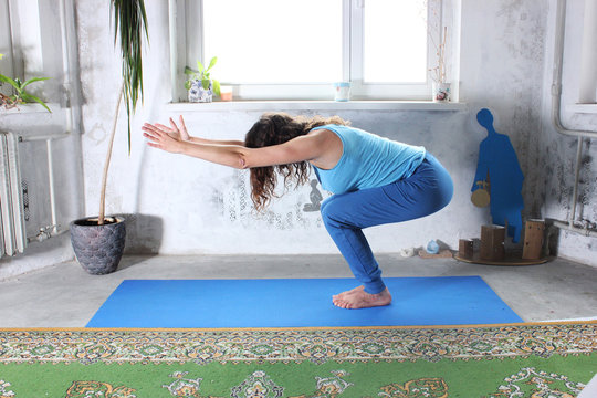 Young attractive smiling woman practicing yoga, sitting in One Legged King Pigeon exercise, Eka Pada Rajakapotasana pose, working out, wearing sportswear, grey pants, bra, indoor full length, home