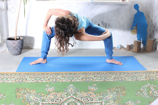 Young attractive smiling woman practicing yoga, sitting in One Legged King Pigeon exercise, Eka Pada Rajakapotasana pose, working out, wearing sportswear, grey pants, bra, indoor full length, home