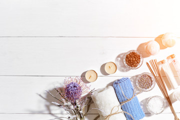 Spa products. Bath salts, dry flowers lavender, soap, candles and towel. Flat lay on white wooden background, top view. Sun flare