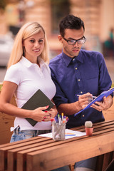 Two young focused students standing outdoors during the break and doing some tasks