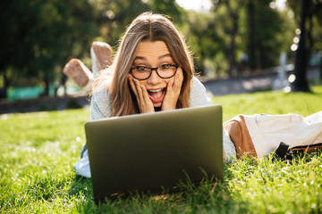 Shocked brunette woman in eyeglasses lying on grass