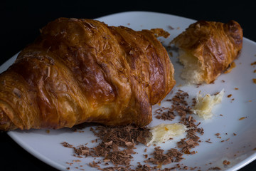 Single Croissant on a white surface with chocolate flakes, angle view