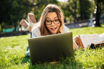 Happy surprised brunette woman in eyeglasses lying on grass