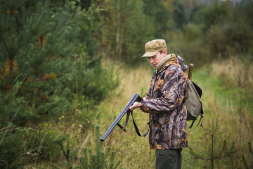 Naklejka premium Hunter with a backpack and a hunting gun in the autumn forest. Man is charging a hunting rifle. 