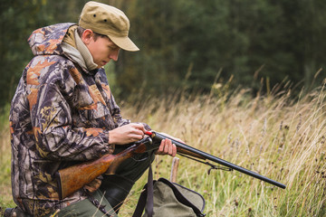 Hunter with a backpack and a hunting gun in the autumn forest. Man is charging a hunting rifle. 
