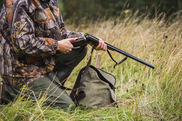 Hunter with a backpack and a hunting gun in the autumn forest. Man is charging a hunting rifle. Close up.