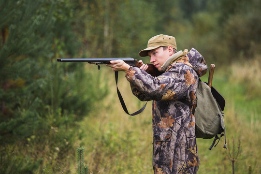 Hunter with a backpack and a hunting gun in the autumn forest. The man is on the hunt. Hunter is aiming.