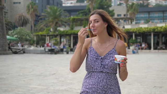 Pretty Young Woman Walks Down The Street And Eat With A Spoon Ice Cream