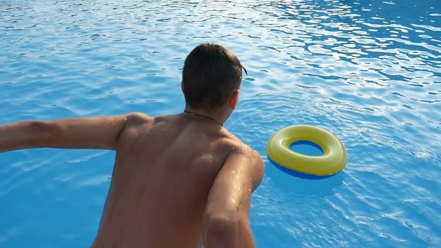 A young sportive man jumps straight into an inflatable yellow and blue ring in the blue sea waters on a sunny day in slow motion. The seascape looks great.