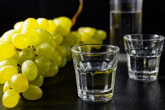 Two glasses and bottle of traditional drink Ouzo or Raki on black dish with a branch of grapes