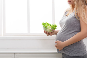 Young pregnant woman eating fresh green salad, copy space.