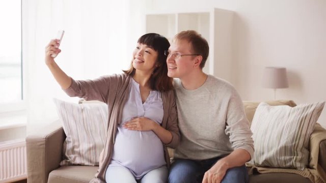 man and pregnant woman taking selfie at home