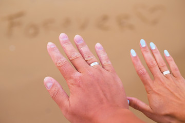 The inscription on the sand forever on the background of the hands of a young couple.