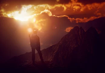 Crédence de cuisine en verre imprimé Alpinisme back lit mountain climber and fiery sunset clouds