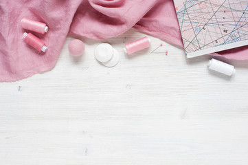 Pink natural fabric and sewing tools on  the white wooden table