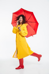 Full length image of surprised happy african woman in raincoat