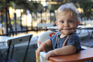 Little boy is sitting in a cafe with a spoon