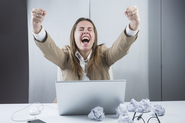 Manager vestita con giacca e camicia,seduta alla sua scrivania esulta per un risultato appena raggiunto. © alex.pin